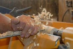 Ein eingespanntes Stück Holz wird bearbeitet und es fliegen Spähne.