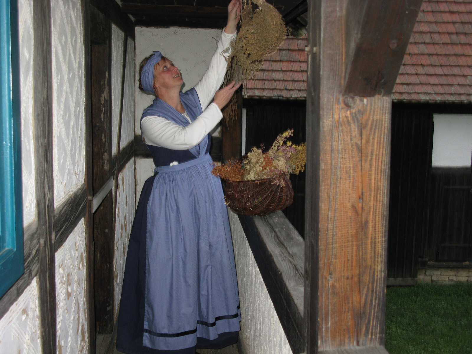 In Tracht steht die Schäfersfrau Minna im Fachwerk-Laubengang und befestigt Trockenblumen.