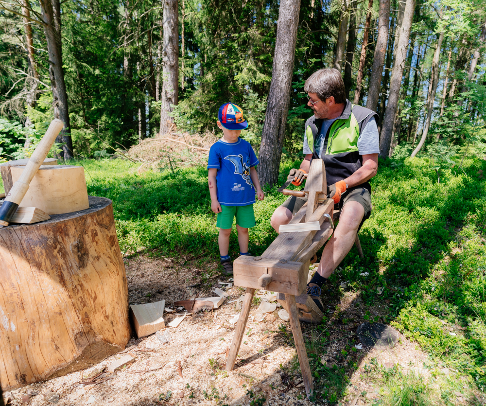 Ein Mann erklärt einem Jungen seine Holzwerk-Station im Wald. 