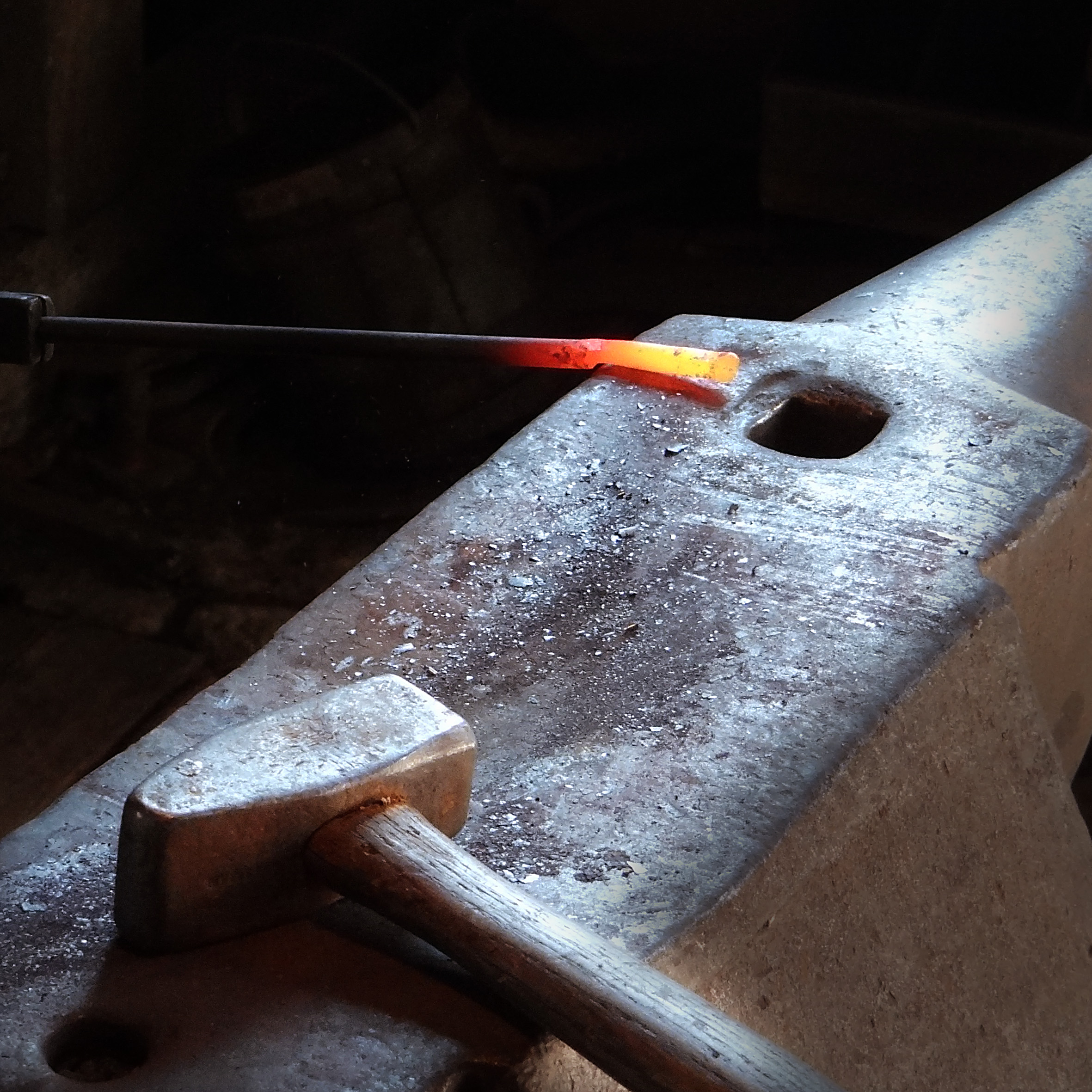Eine glühende Stahlstange und ein Hammer liegen auf dem Amboss.