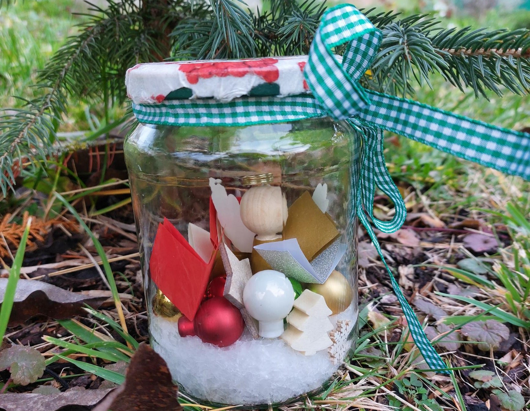 Einkochglas mit weihnachtliche Deko innendrin vor einem Nadelbaum