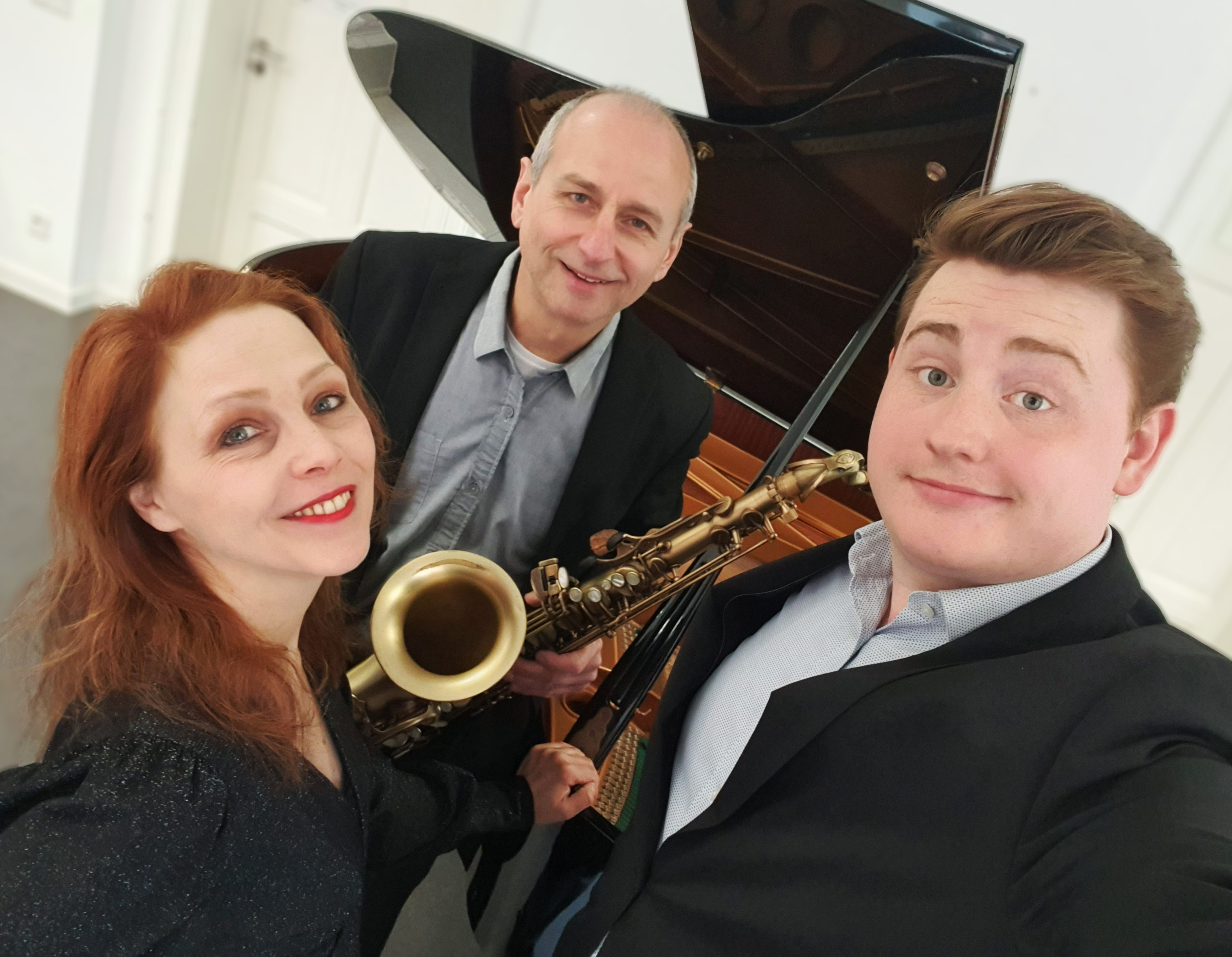 Eine Sängerin und zwei Musiker, einer hält ein Saxophon, vor einem PIa