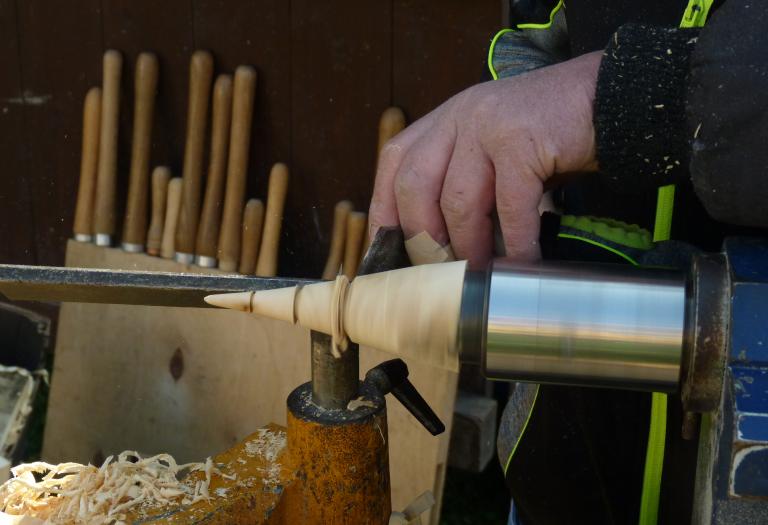 Ein Holzkegel wird gedrechselt. Daneben liegen Holzspäne.