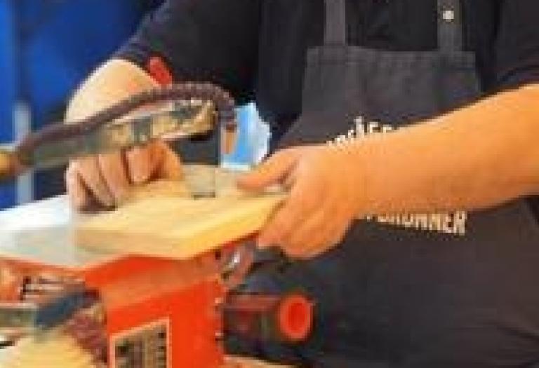 Ein Holzbrett ist in einer Laubsäge eingespannt. 