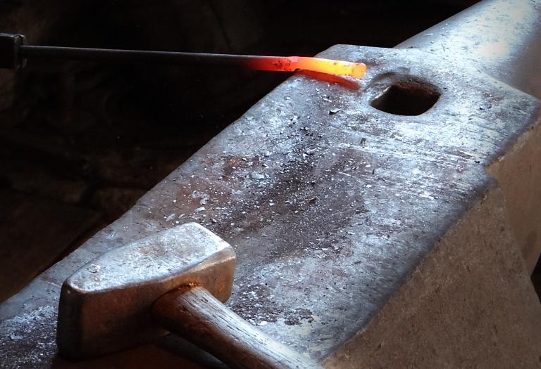 Eine glühende Stahlstange und ein Hammer liegen auf dem Amboss.